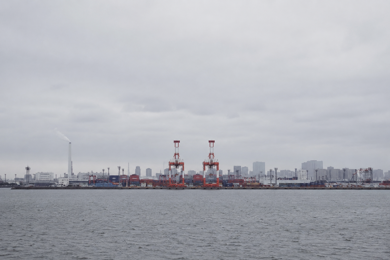 曇天の港湾を写した元写真。手前に水面、中央に赤いガントリークレーン2基とコンテナ、左側に煙突がある